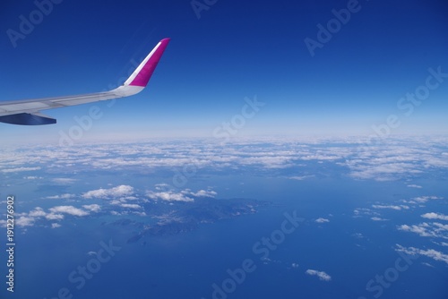 View from an airplane window over white clouds and blue ocean with a wing