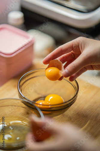 Принти на полотні Close-up of hands separating bright yellow egg yolks into a clear glass bowl for cooking and baking preparation