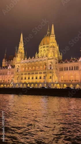 The Hungarian Parliament Building (Országház) is a stunning neo-Gothic landmark on the Pest side of the Danube River in Budapest, completed in 1904, night vertical video.