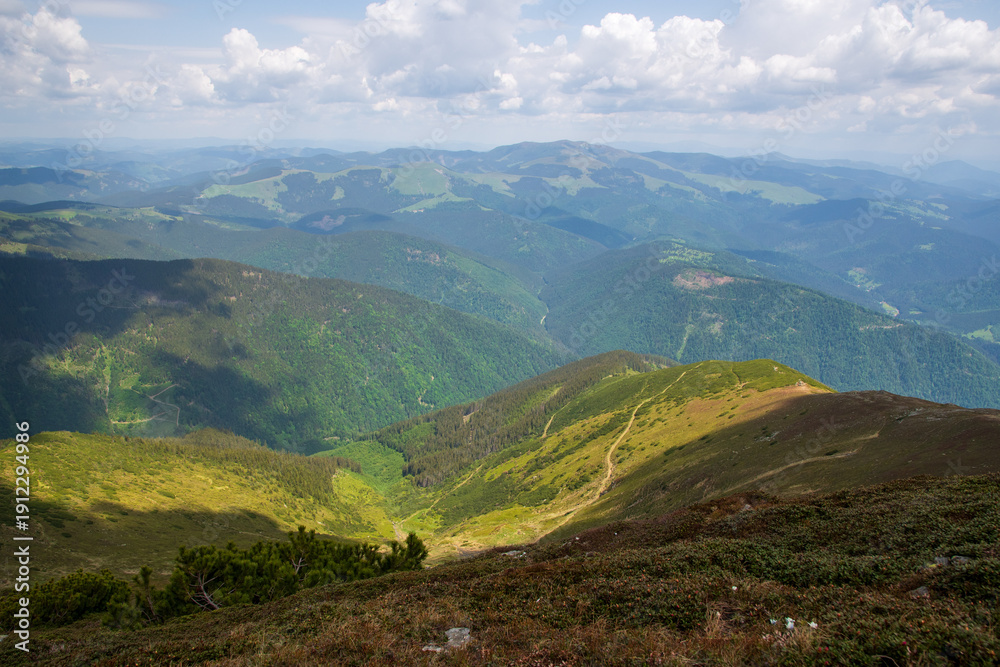 Obraz premium Panoramic view of green mountain ridges and valleys under a partly cloudy summer sky
