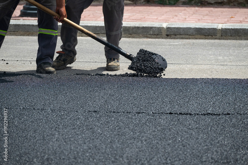 Close-up detail shot of a worker smoothing freshly laid hot asphalt with a shovel.