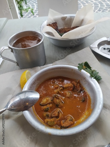 Traditional mussel stew served in white bowl with lemon and fresh herbs.