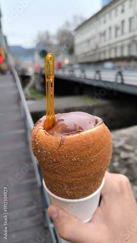 Hand holding traditional chimney cake dessert near a European city canal.