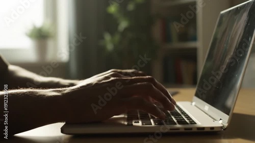 Close-up of hands typing on a laptop in a softly lit room with plants and books in the background