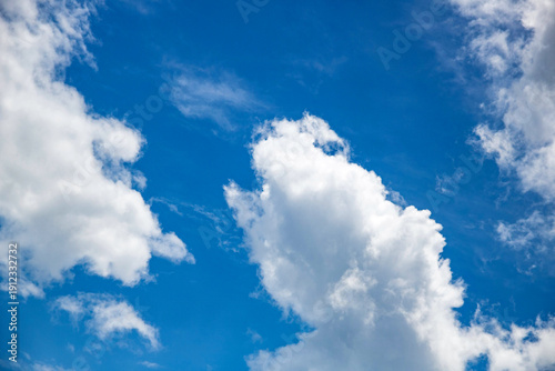 Large, billowing cumulus clouds dominate the foreground against a clear blue sky. These 