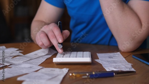 Hands Calculating Tax Totals Among Receipts, Calculator And Pen On Wooden Table, Blue Shirt Sleeve, Busy Scene Of Selfemployed Bookkeeping And Tax Preparation, Focus On Deductions