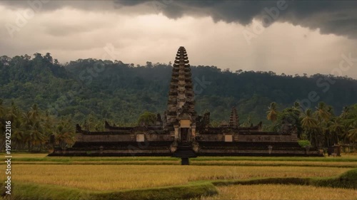 Ancient balinese temple standing amidst golden rice fields under storm clouds with lightning strike over lush tropical mountain