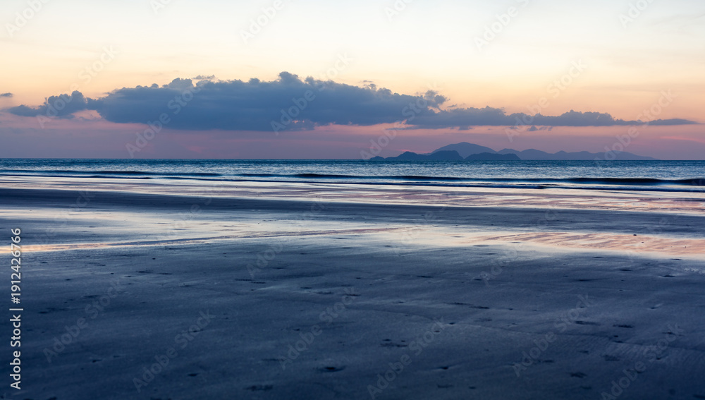Obraz premium Tropical beach at Koh Tarutao, Ao Son Beach, Thailand. Sunrise over the Andaman Sea. Wide sandy shore and calm ocean waves. Cloudy sky with soft morning light.