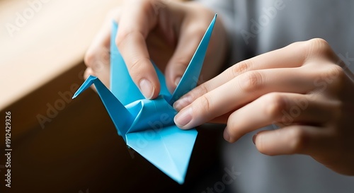 A person creating a bright blue origami crane with bare hands detail