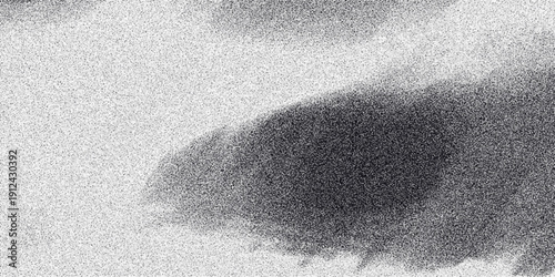 Abstract grayscale image with a large, soft-edged dark form against a speckled grainy background, creating a moody and atmospheric visual