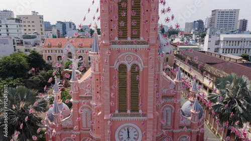 Aerial drone view of the iconic pink church in Ho Chi Minh City, Vietnam. Historic cathedral architecture surrounded by dense urban skyline and modern city buildings.