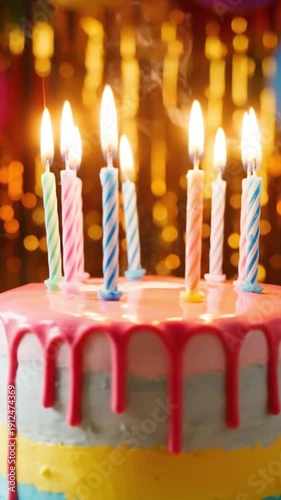 Close up of a colorful layered birthday cake topped with brightly burning striped candles ready for making a celebratory wish during a festive occasion