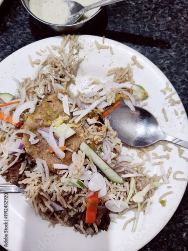 A plate of rice with chicken biryani eating with someone spoon