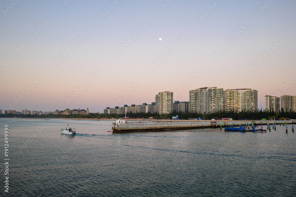 Fototapeta premium Boats at sunset in Qingshuiwan Bay with Lingshui cityscape, Hainan Island, China