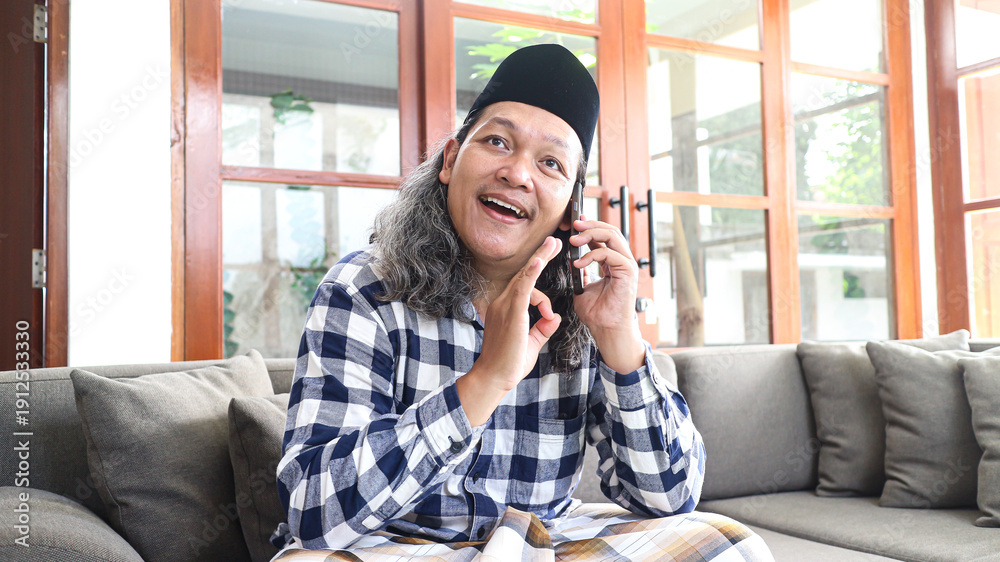 Obraz premium Asian moslem man making a phone call to family and friends to say grace during Idul Fitri celebration