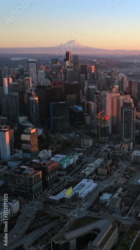 Aerial panorama of Seattle Washington skyline with Mount Rainier on the horizon at sunset, revealing dense urban core, modern high rises and expansive coastal waterways.