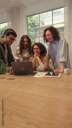 Diverse business people gathered around a laptop in a bright office reviewing charts together. Team collaboration strategic discussion focused planning and modern workplace communication.