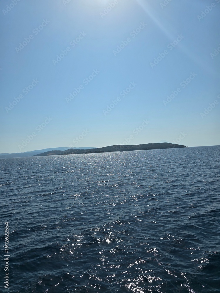 Naklejka premium Sparkling blue ocean water with sun glint and distant island silhouette