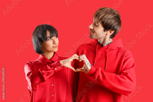 Young couple making heart with hands on red background. Valentine's day celeb...
