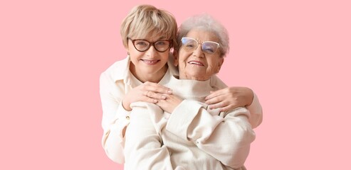 Happy woman and her senior mother hugging on pink background