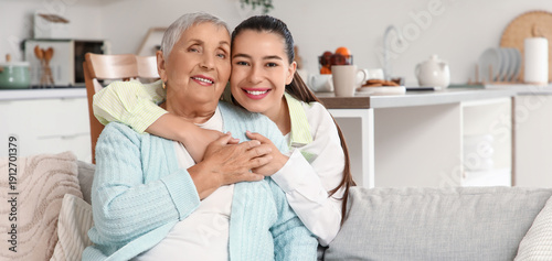 Young woman hugging her grandmother on sofa at home