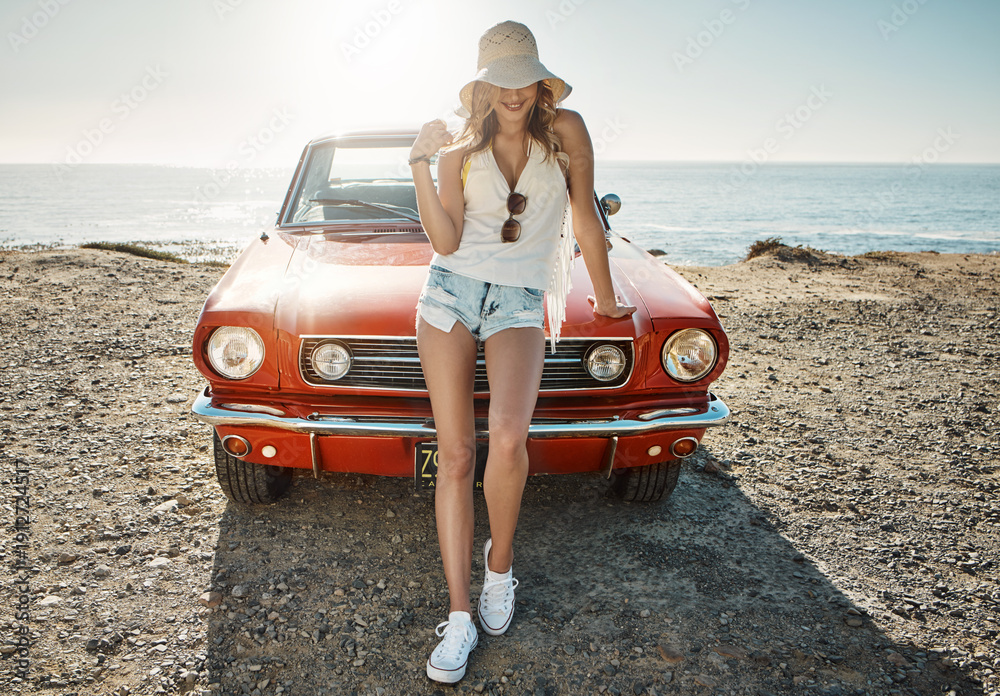 Fototapeta premium Beach, travel and woman with muscle car for road trip, summer fashion or vacation in nature. Vintage vehicle, holiday and person by sea with stylish tourist, smile and adventure on hood of transport