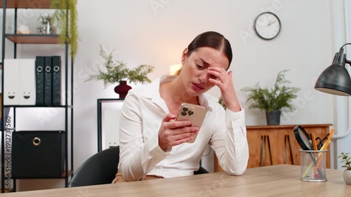 Young businesswoman at home office looks at smartphone sees game loss failed order budget blown and frowns. Freelancer girl at table reads client rejection checks bill notes risk and plans next step.