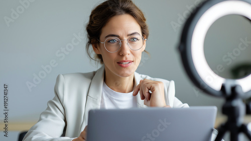 Wallpaper Mural Woman wearing glasses recording video while sitting at laptop with ring light setup. Torontodigital.ca