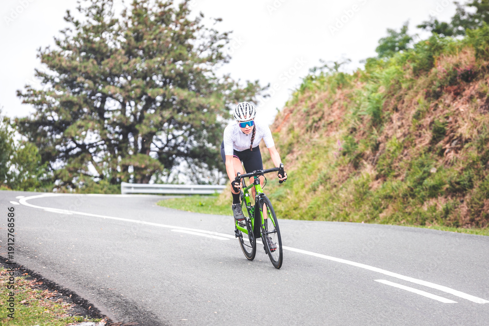 Fototapeta premium Young caucasian woman going downhill on a corner with a road bike on an asphalt road of a mountain.