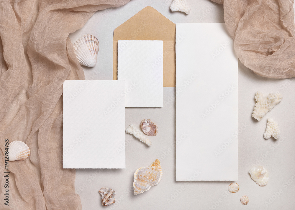 Fototapeta premium Cards and envelopes on beige stone with seashells top view, mockup. Coastal wedding stationery set