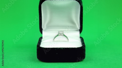 A diamond ring is displayed in an open black jewelry box on a green background.