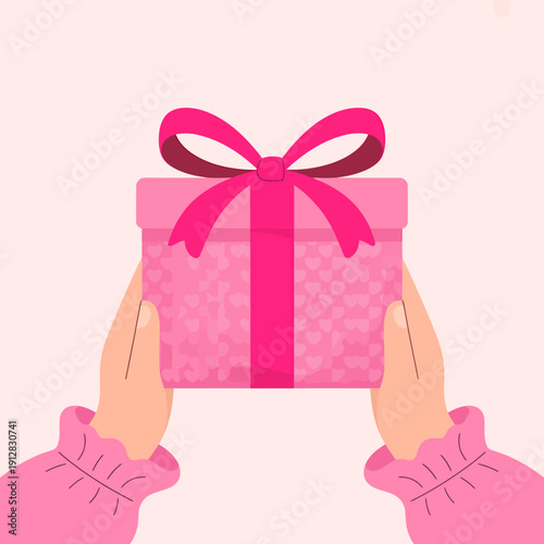 Hands holding a pink gift box with a bow on top