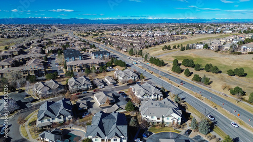 Roadway near E 470 shows active lane work by neighborhoods leading toward wide open greenspace. Bright cones, mixed shingles, pale winter vegetation shape transitional suburban view, Aurora, CO