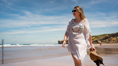 Beautiful middle-aged woman enjoying walk on sandy beach Monte Clerigo in Portugal on sunny summer day. Front view	
