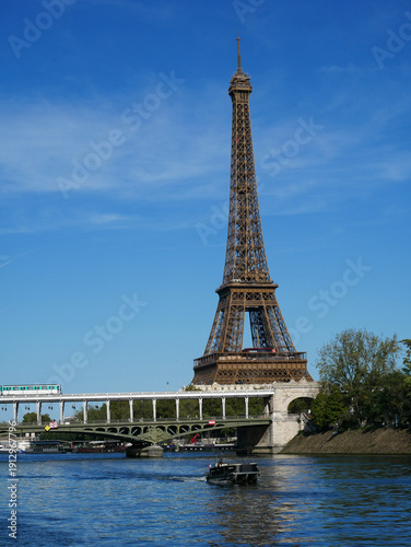 Eiffel Tower with Line 6 metro train on Bir-Hakeim Bridge over Seine, Paris: green RATP viaduct against blue sky, iconic urban view from Passy side. 