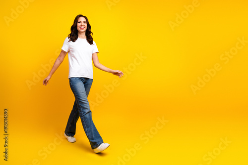 Foto Young woman in tshirt and jeans walking confidently against a bright yellow back