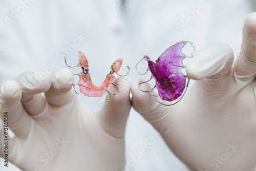 Orthodontist hands in medical gloves holding two colorful removable dental plates for upper and lower jaw, professional pediatric dentistry and orthodontic treatment concept