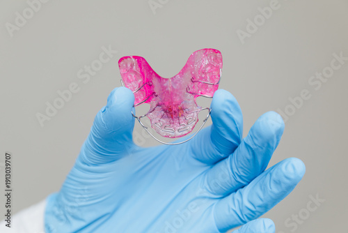 Orthodontist in blue medical glove holding pink removable dental plate for teeth alignment, professional pediatric dentistry and orthodontic correction concept
