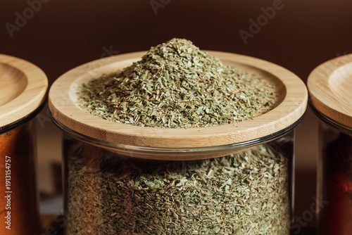 oregano in glass bottle . The seasoning lies on a wooden lid.