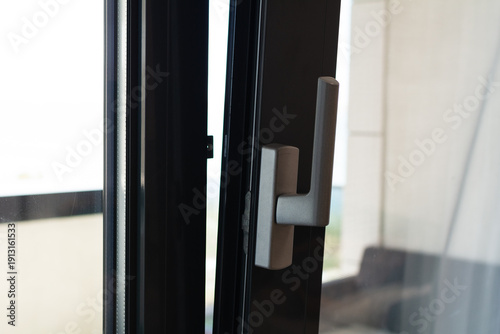 PVC window handle. PVC patio door. Close-up of a slightly open metal or PVC balcony door. Selective focus, shallow depth of field.