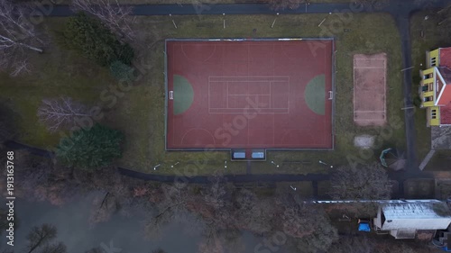 Aerial tennis court overview sports facilities. The video shows a rectangular court with lines and nets. It features surrounding greenery and a building