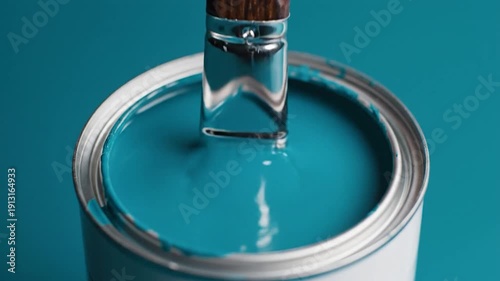 Paintbrush dipped in vibrant teal paint can close up