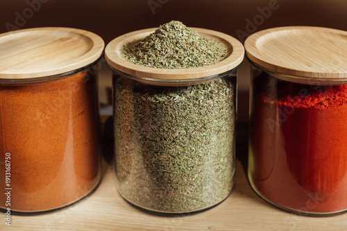 oregano in glass bottle . The seasoning lies on a wooden lid.