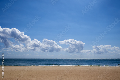Peaceful landscape of the wide sandy Haeundae Beach under a bright blue sky with scattered white clouds in Busan, South Korea, during a calm afternoon.