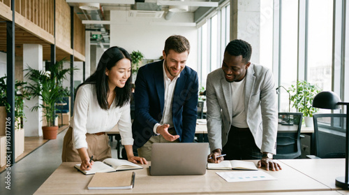 Three colleagues leaning over laptop in bright contemporary office. Multiracial teamwork, creative discussion, productivity and business growth concept.