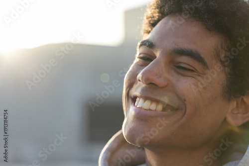 Tableau sur toile African American man smiling under warm backlight on rooftop, wearing hoodie wit