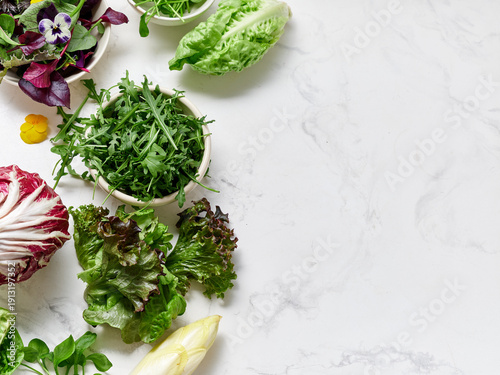 Fresh variety of lettuces and colorful vegetables on marble countertop ready for salad preparation and healthy meal ideas