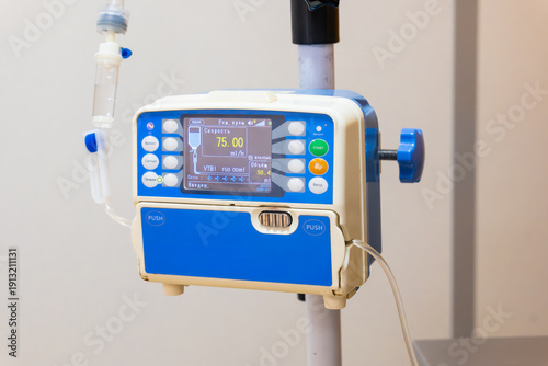 Blue veterinary IV infusion pump mounted on pole with fluid bag and digital screen displaying metrics, close-up detail against blurred background