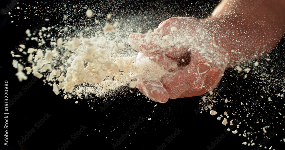 Fototapeta premium Close-up of baker’s hand throwing flour against black background. Dramatic flour explosion captured in high detail, baking and culinary preparation concept.