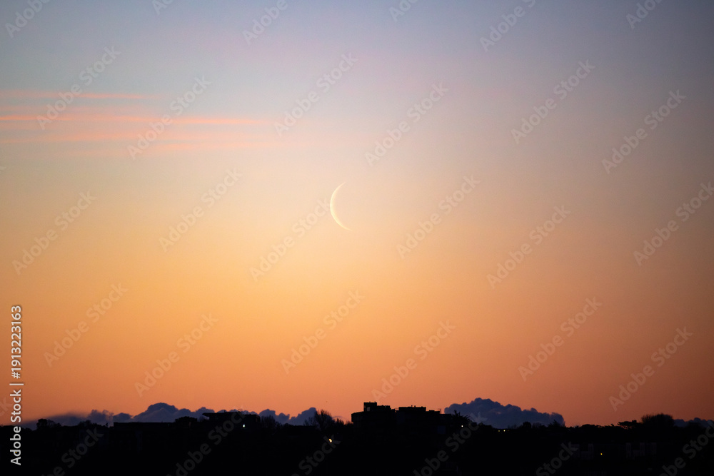 Fototapeta premium Crescent moon rising at dawn over south Dublin against a golden orange sky